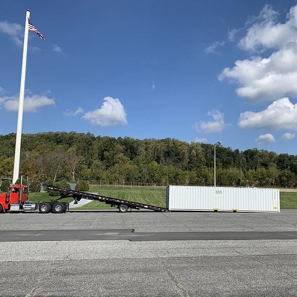 Red semi-truck with trailer and white shipping container in parking lot under a blue sky.
