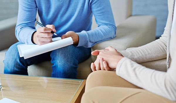A man and two women are sitting on a couch talking to each other.