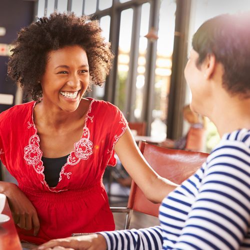 Two women are sitting at a table with a stack of books.