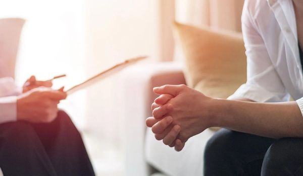 A woman is sitting on a couch talking to a doctor.