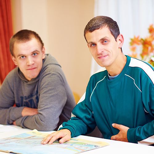 Two men are sitting at a table with one wearing a sweatshirt that says ' jackson ' on it