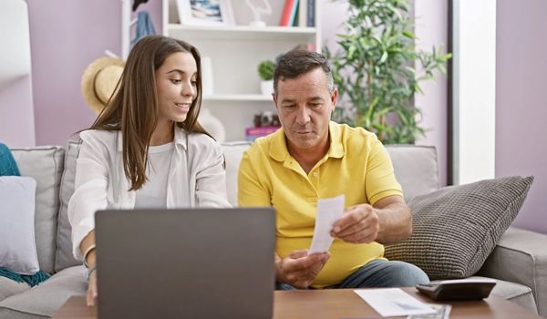 A man and a woman are sitting on a couch looking at a laptop.