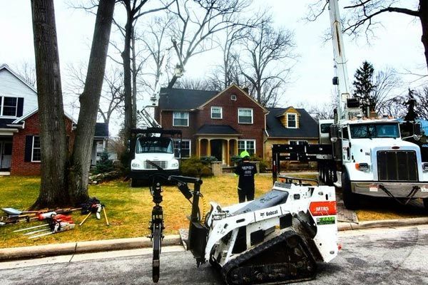 Snowy residential street with a tow truck, parked cars, and damaged vehicles near houses
