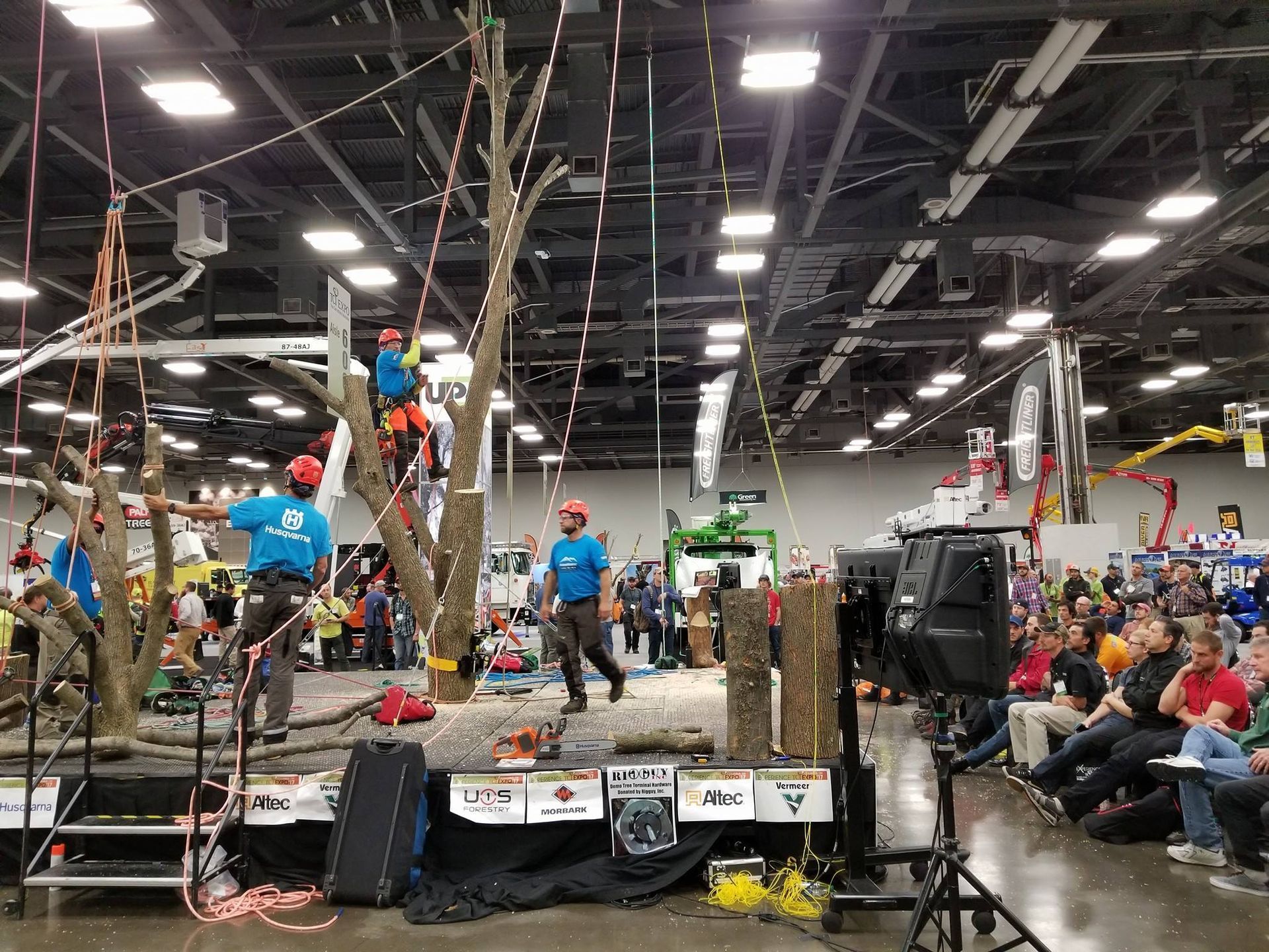 Indoor climbing competition with climbers on a wall and spectators seated nearby