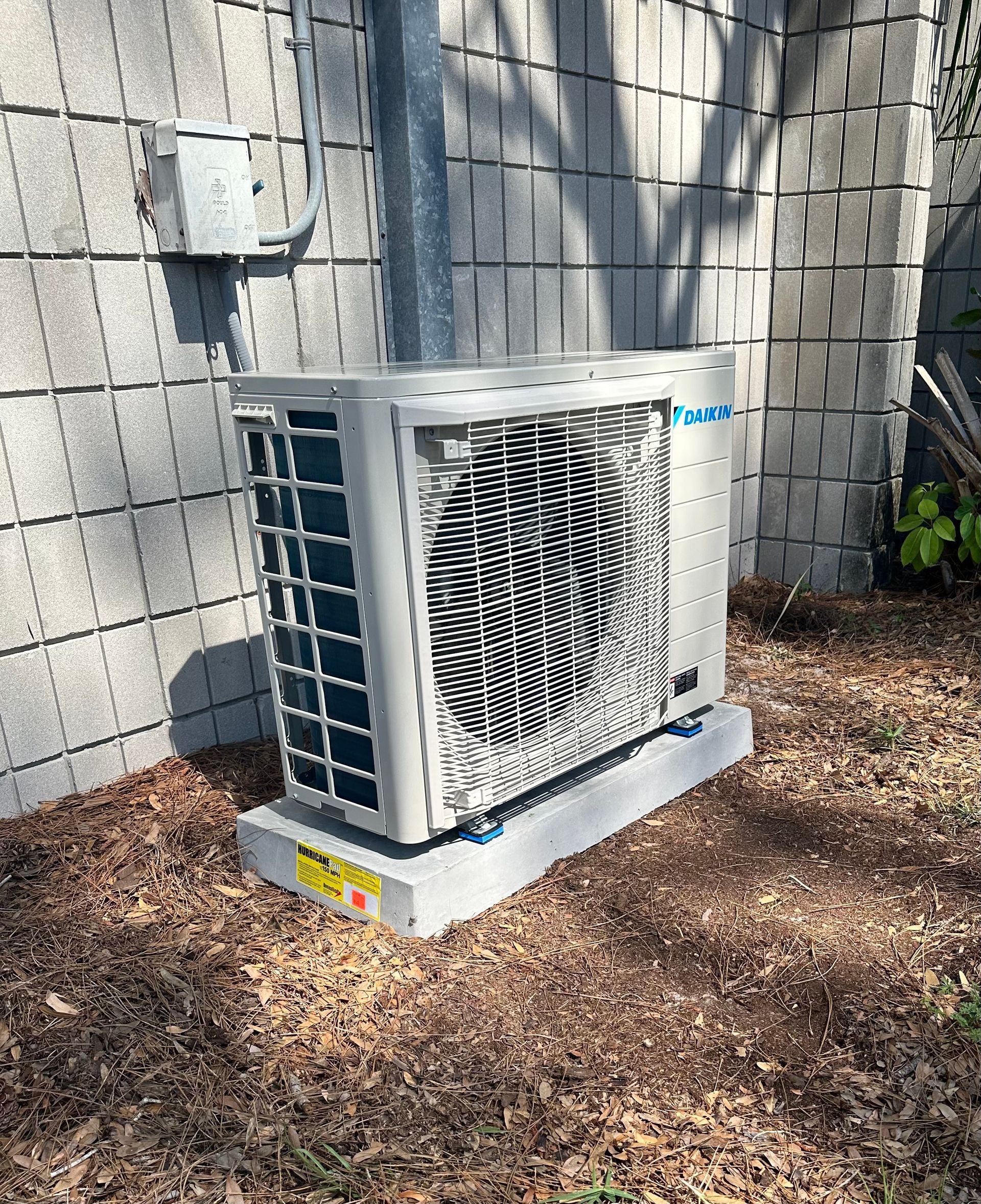 A large air conditioner is sitting on top of a pile of mulch next to a brick wall.