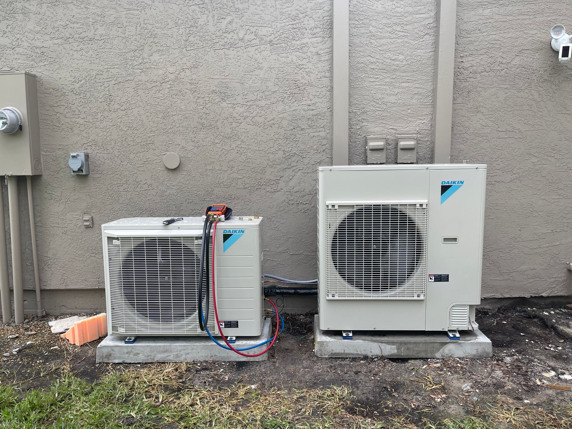 Two air conditioners are sitting next to each other on the side of a building.