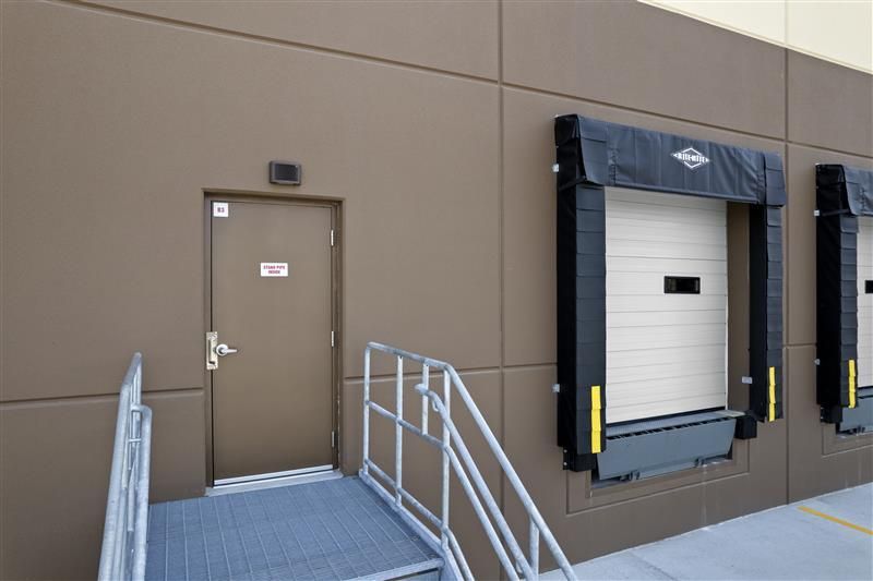 Brown industrial building with loading docks, a side door, and a ramp.