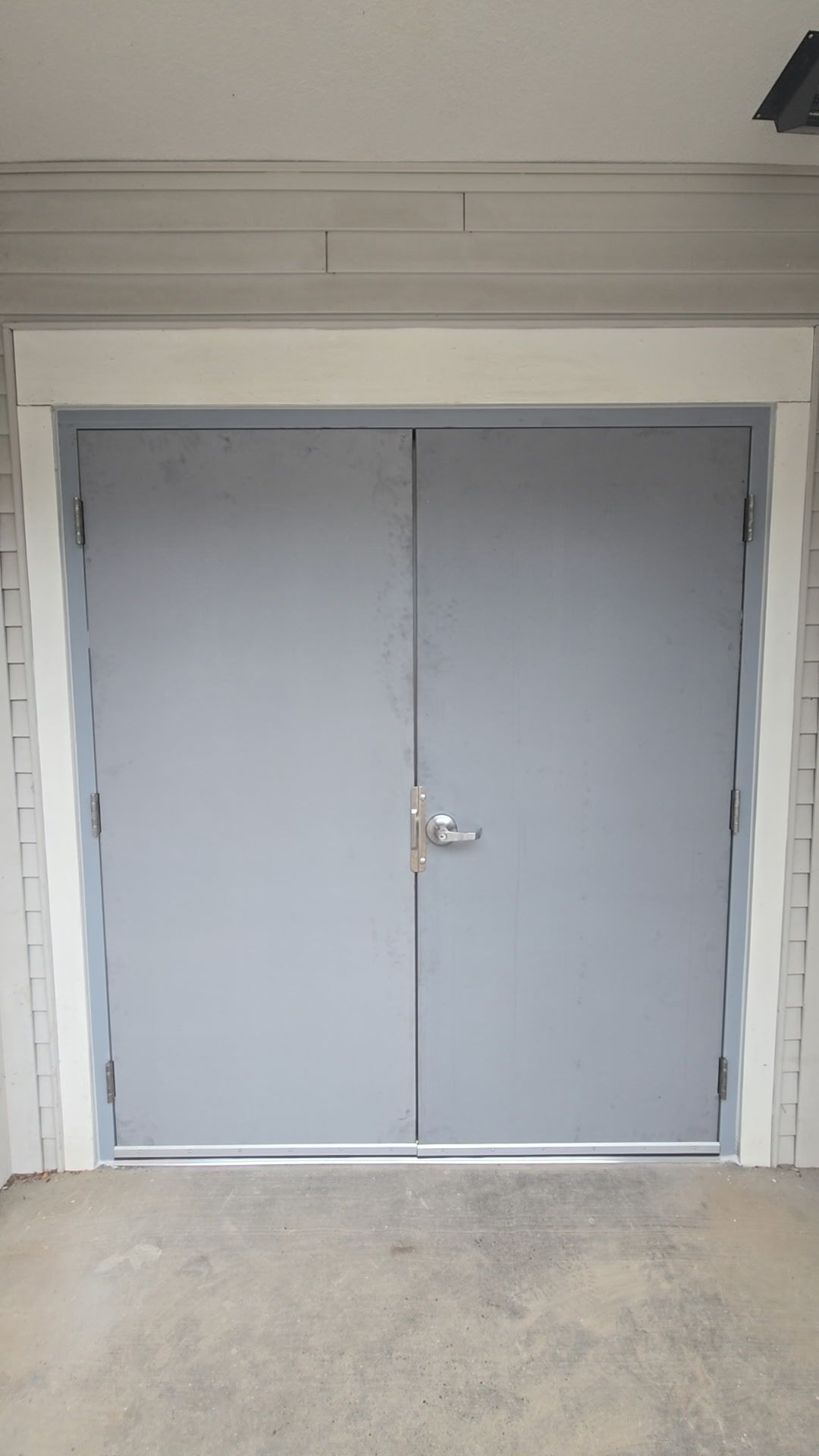 Double gray doors, centered, with a silver handle, set in a white-trimmed opening, on a concrete surface.