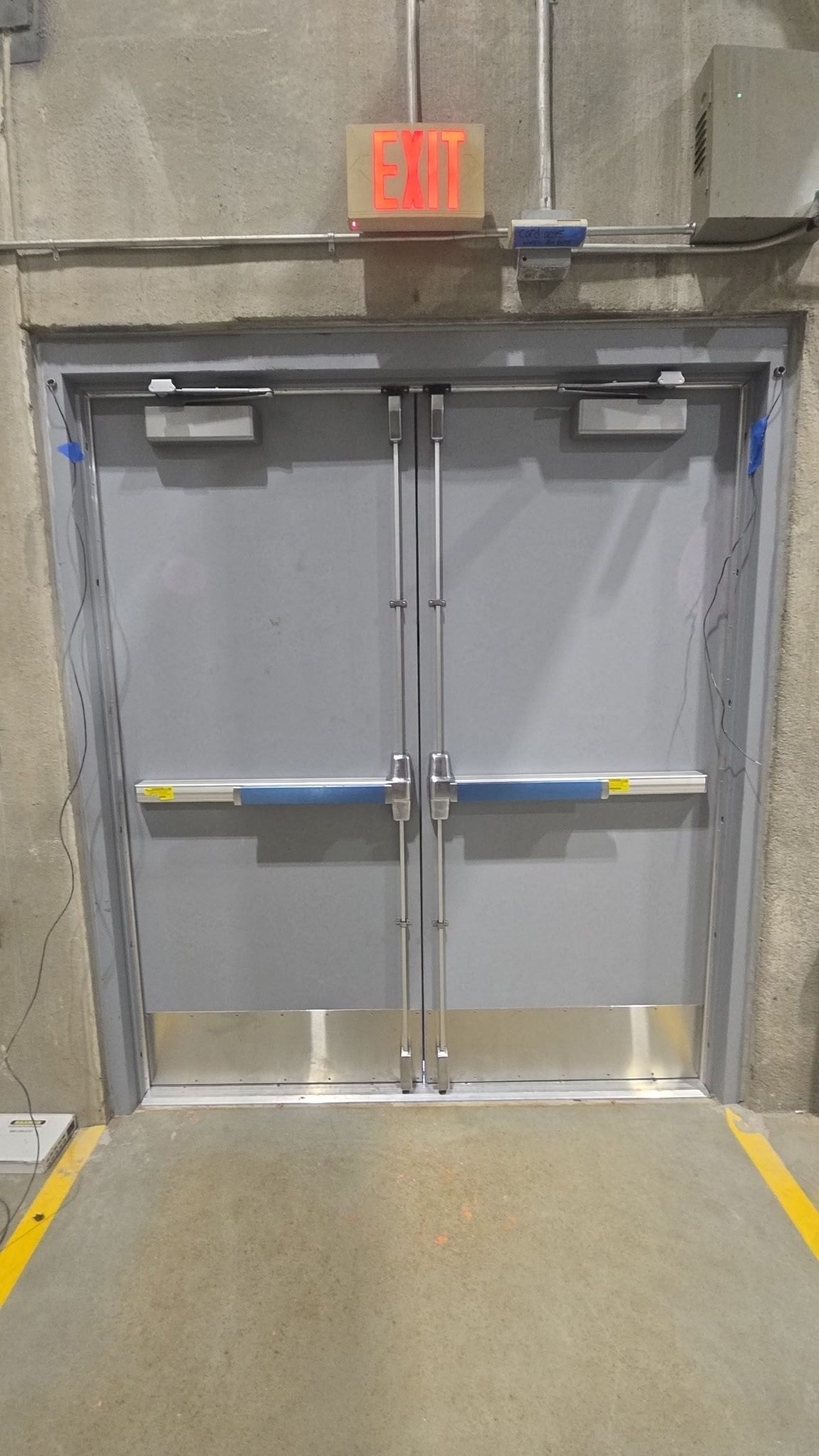 Double gray doors with push bars and an exit sign above.