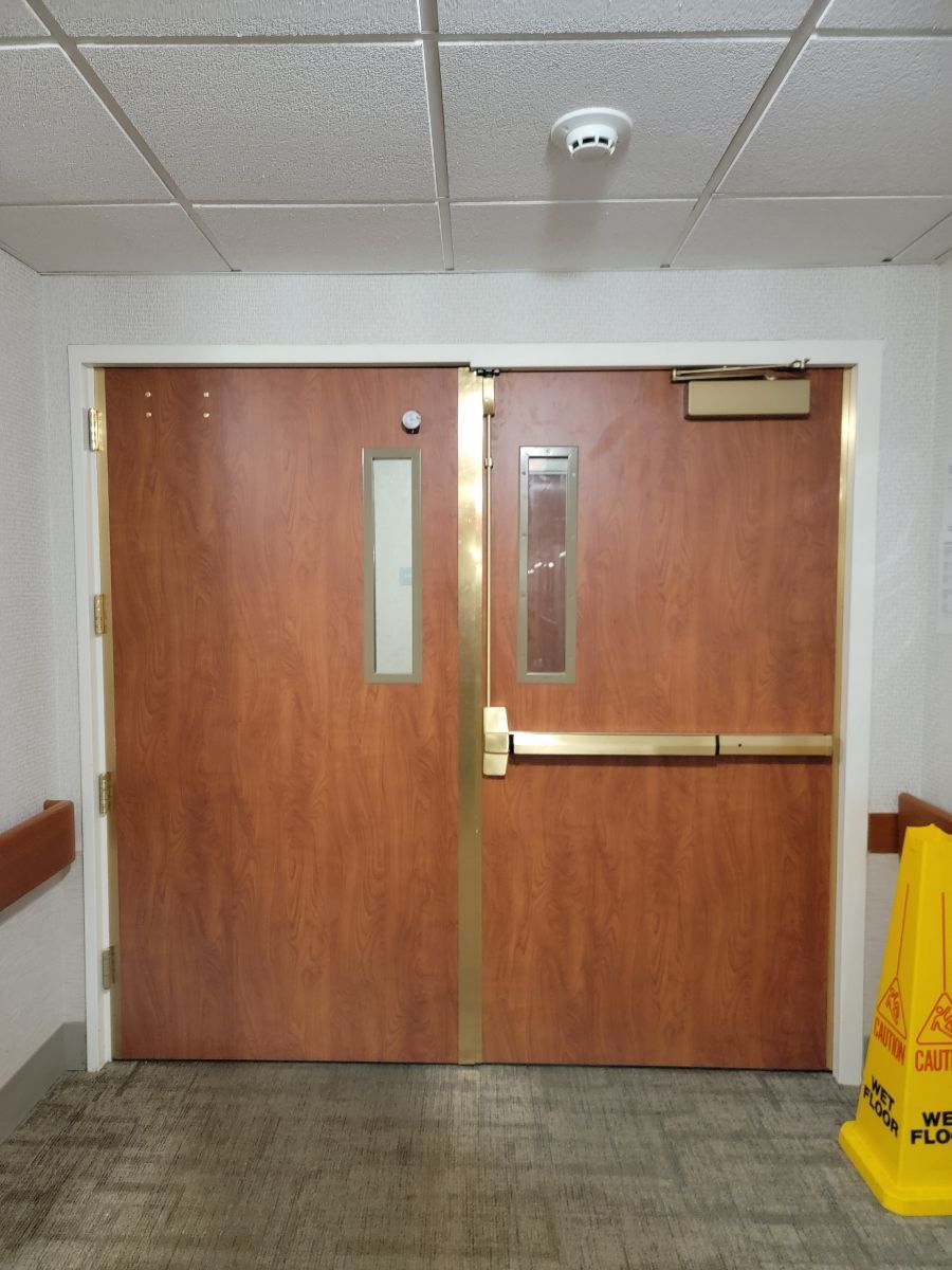 Double wooden doors with rectangular windows and brass hardware; hallway.