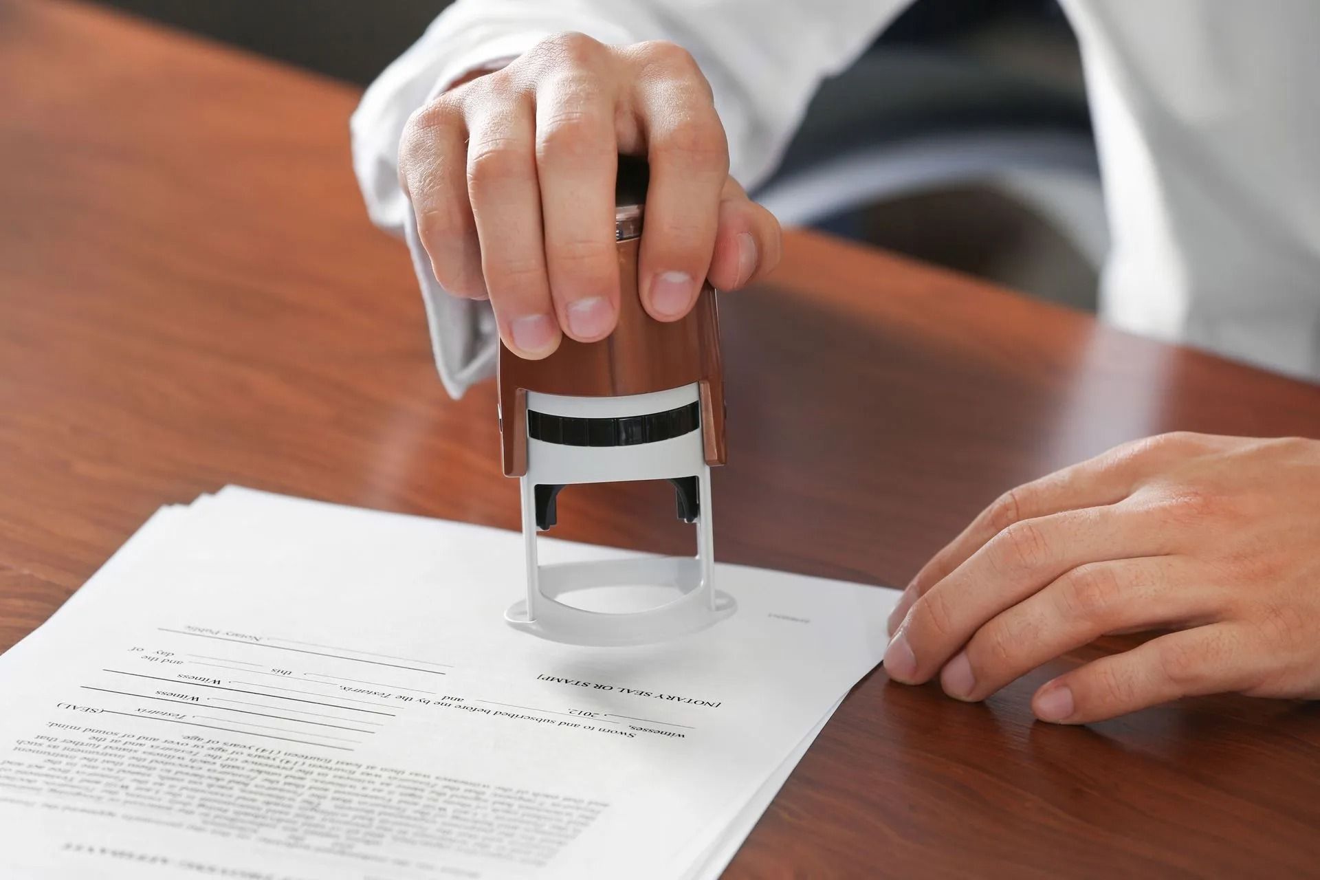 Person stamping a document with a brown and black stamp on a wooden desk.