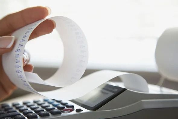 Hand holding a long paper receipt over a calculator.
