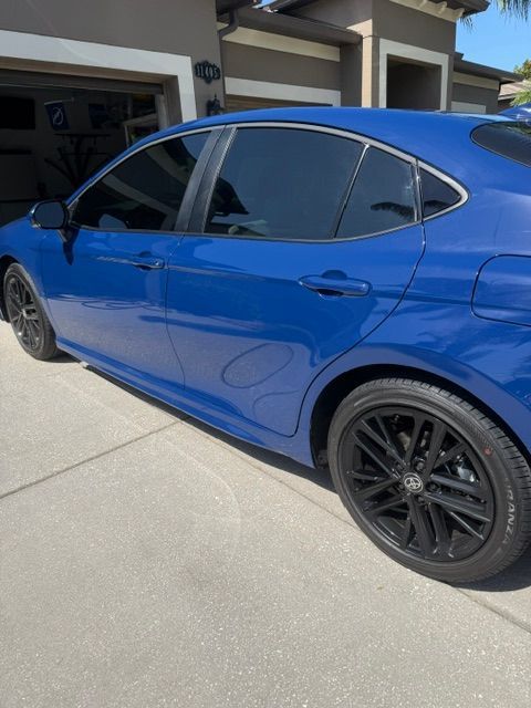 Blue sedan parked in a driveway beside a garage, shown from the side.