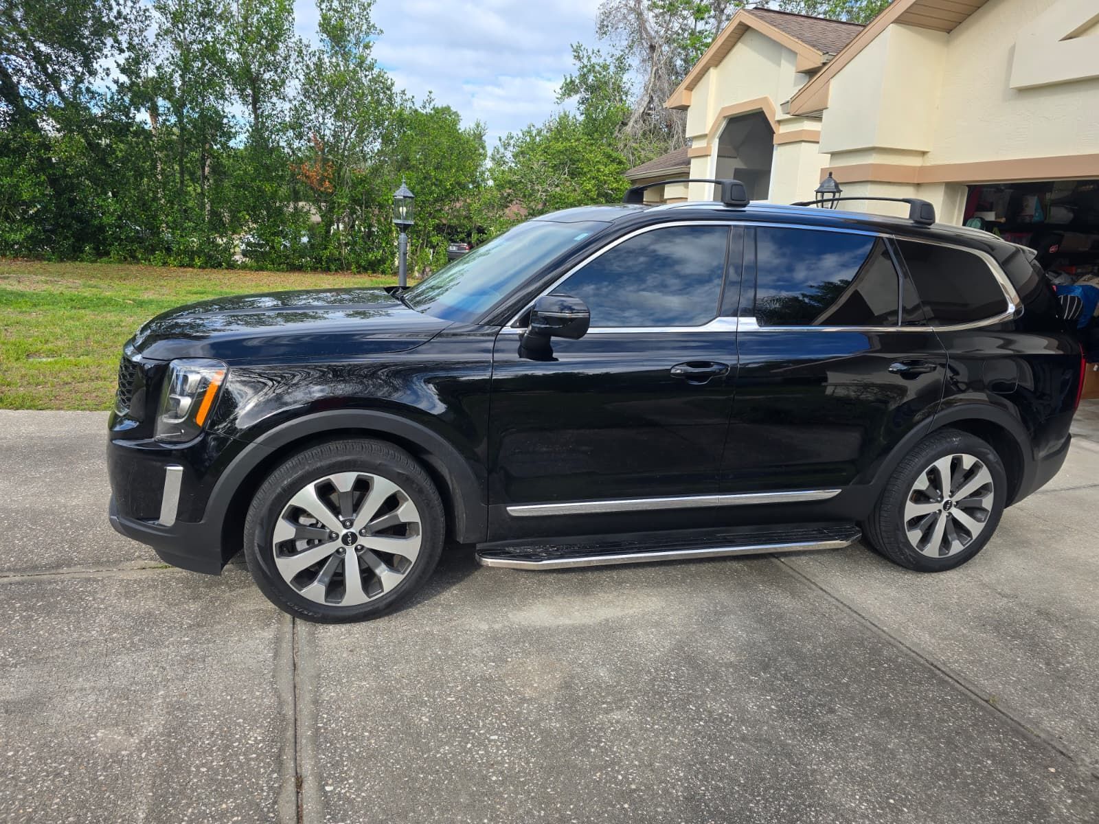 A black Kia Telluride SUV parked in a residential driveway on a sunny day