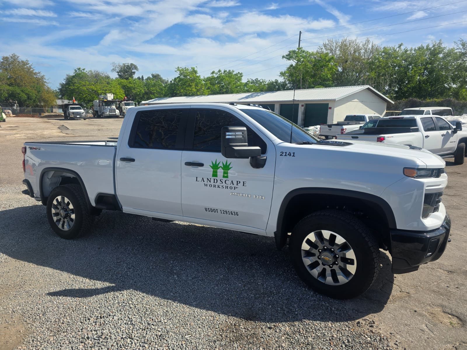 A white pickup truck with a business logo featuring green hands is parked on a gravel lot under a sunny sky