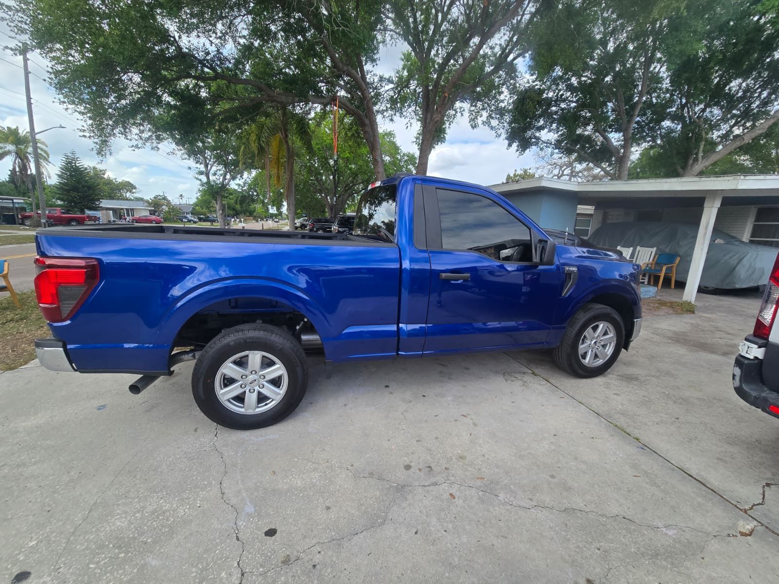 A blue Ford pickup truck parked on a concrete driveway near a house and trees