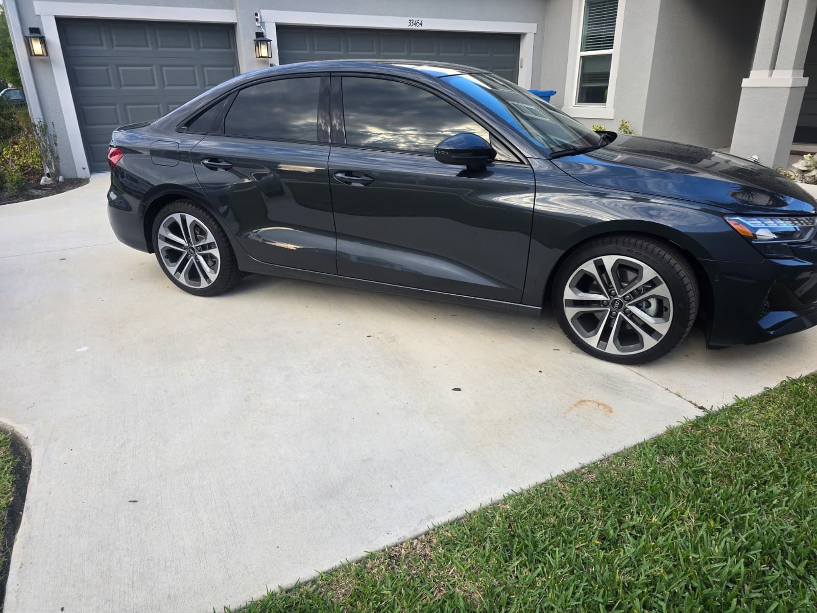 A dark gray sedan parked in a concrete driveway in front of a house with two garage doors