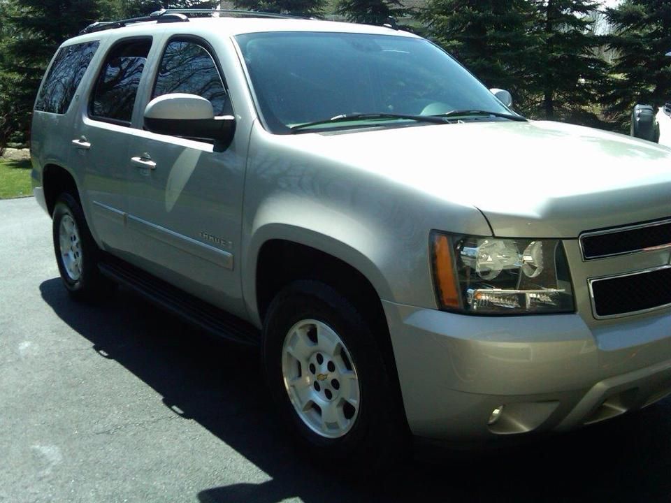 A silver suv is parked in a driveway with trees in the background