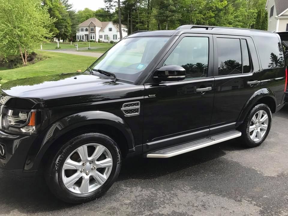A black land rover discovery is parked in a driveway in front of a house.