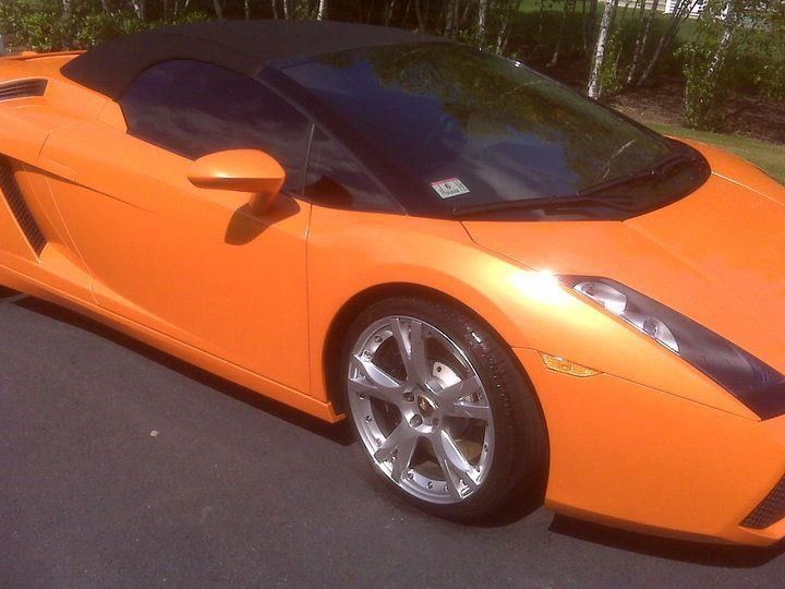 An orange sports car with a black top is parked on the street