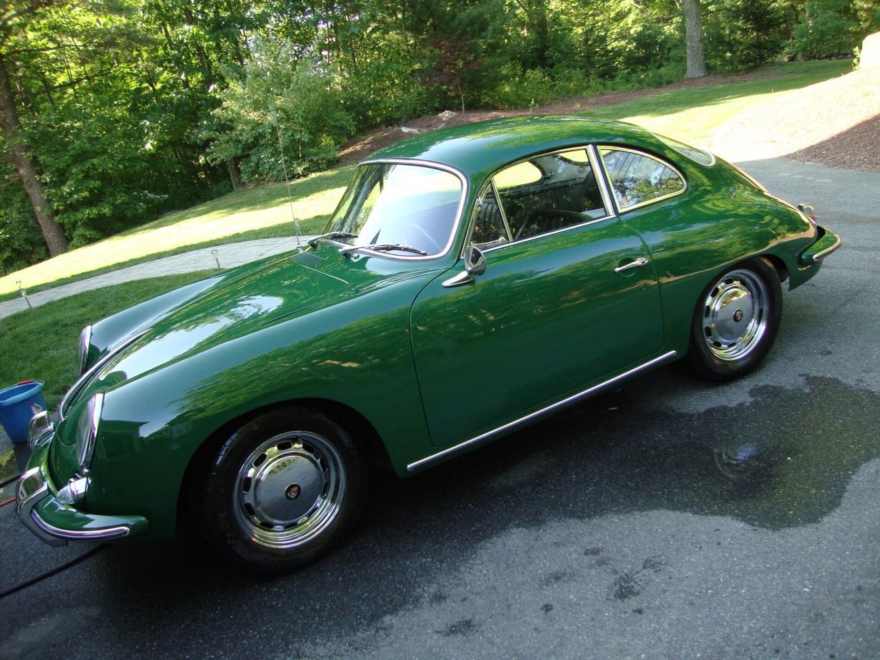 A green porsche is parked in a driveway with trees in the background