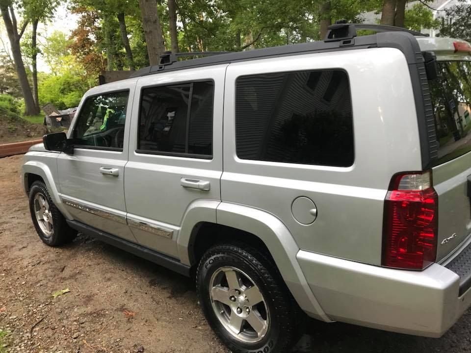 A silver jeep is parked in a driveway next to trees.