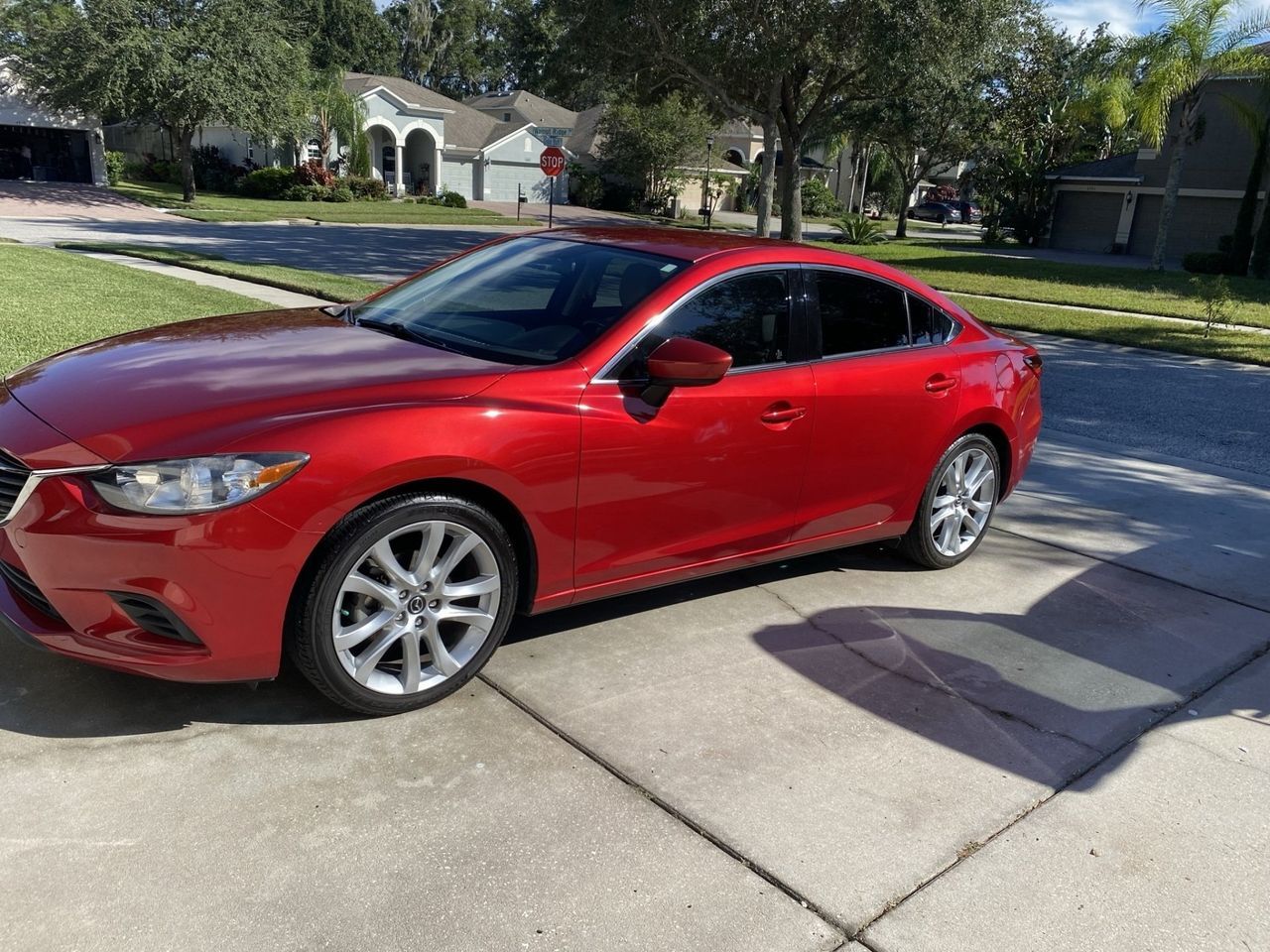 A red car is parked on the side of the road in a driveway.