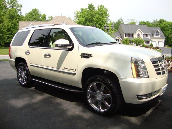 A white cadillac escalade is parked in front of a house