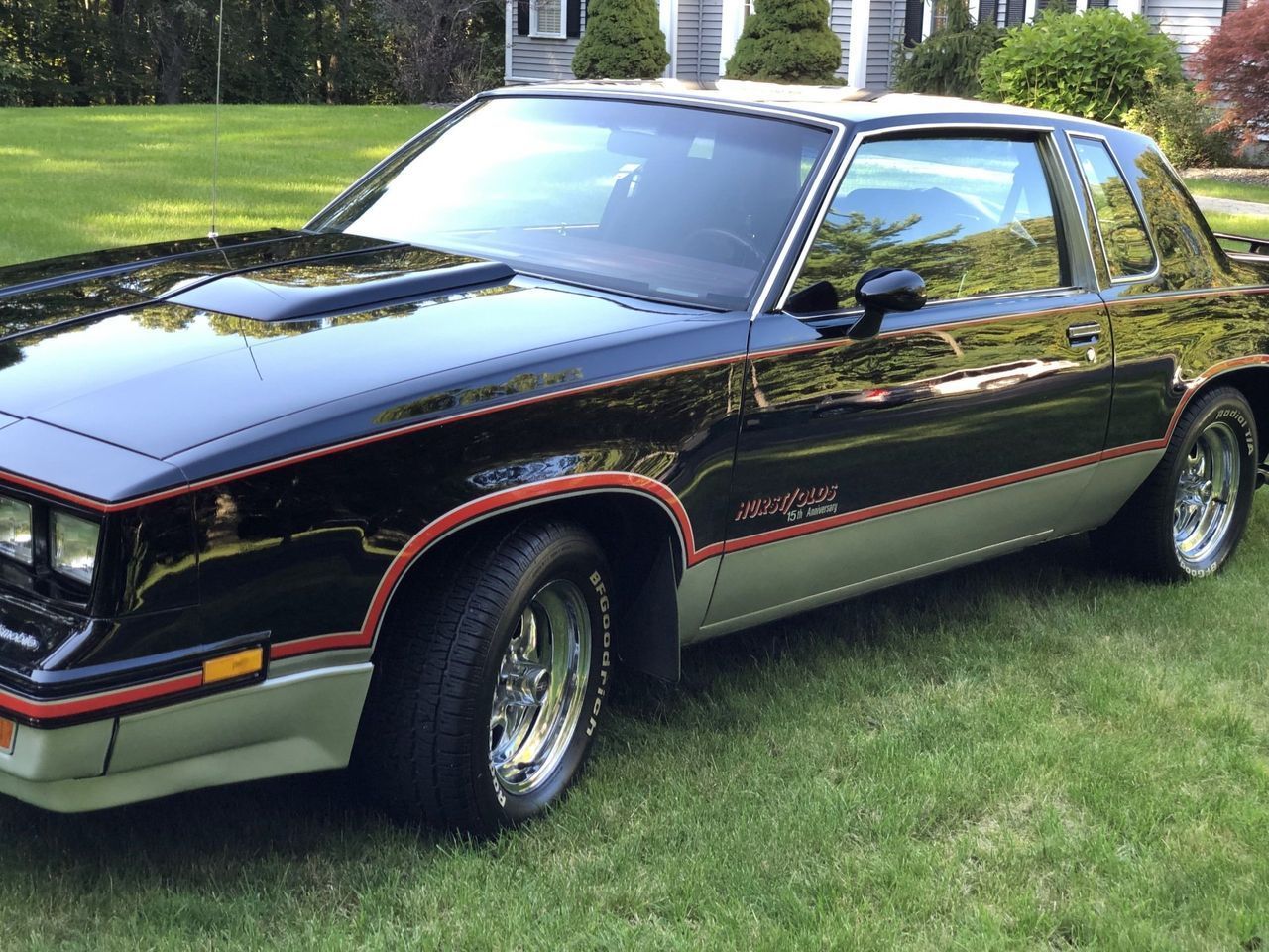 A black car is parked in the grass in front of a house.