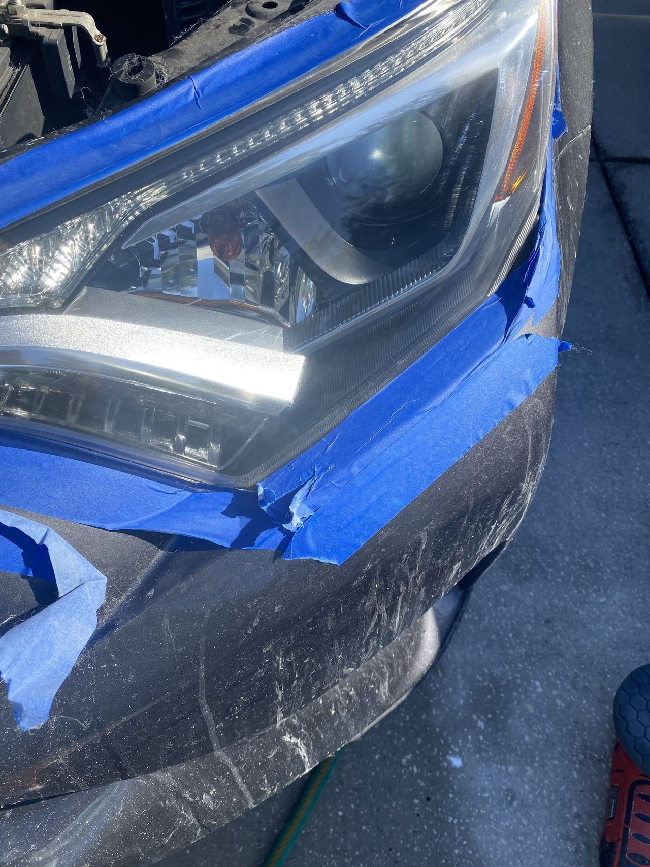 A close up of a car 's headlight with blue tape on it.