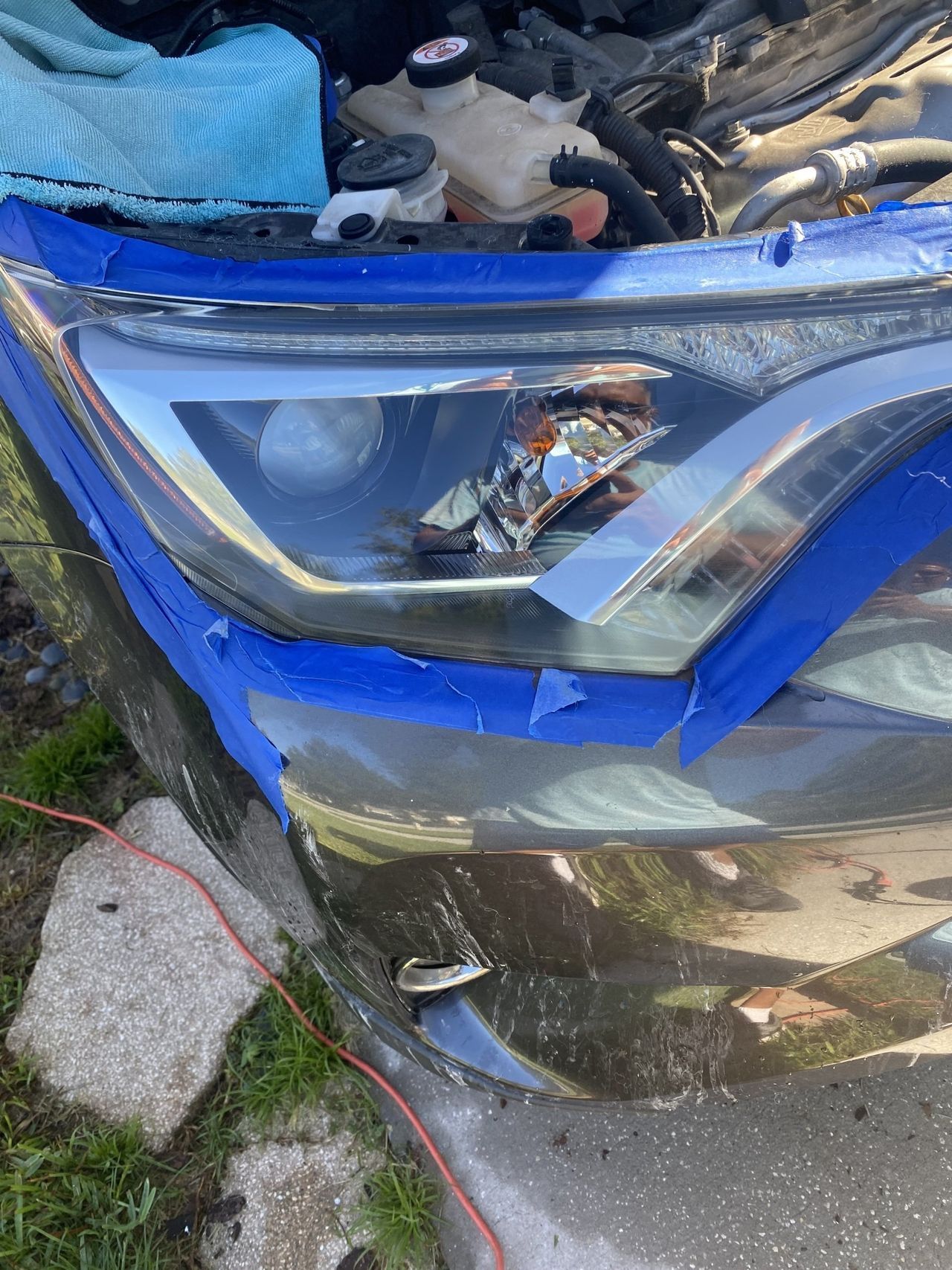 The headlight of a car is taped with blue tape.