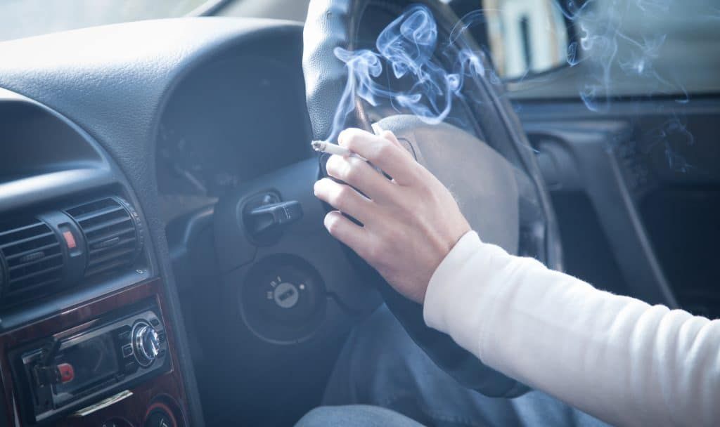 Person holding a lit cigarette while driving a car. Smoke visible.