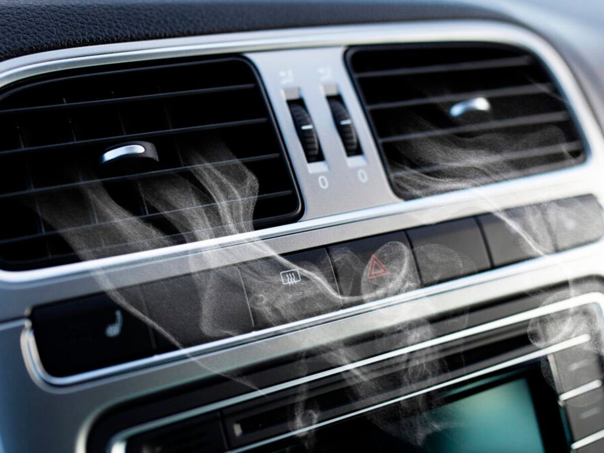 Close-up of car dashboard vents with visible vapor, suggesting a malfunction. Silver and black interior.