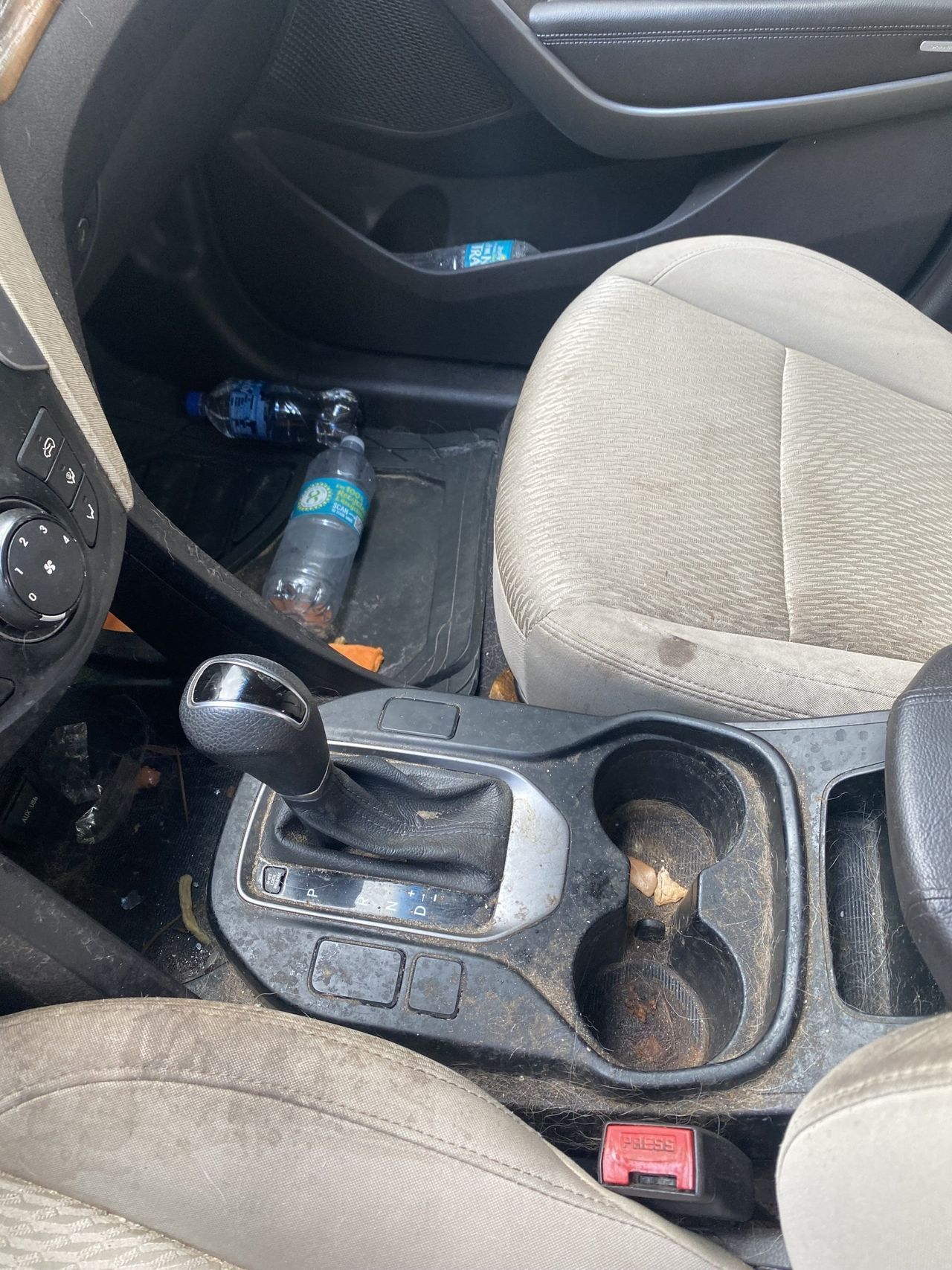 A dirty car with a bottle of water in the center console.