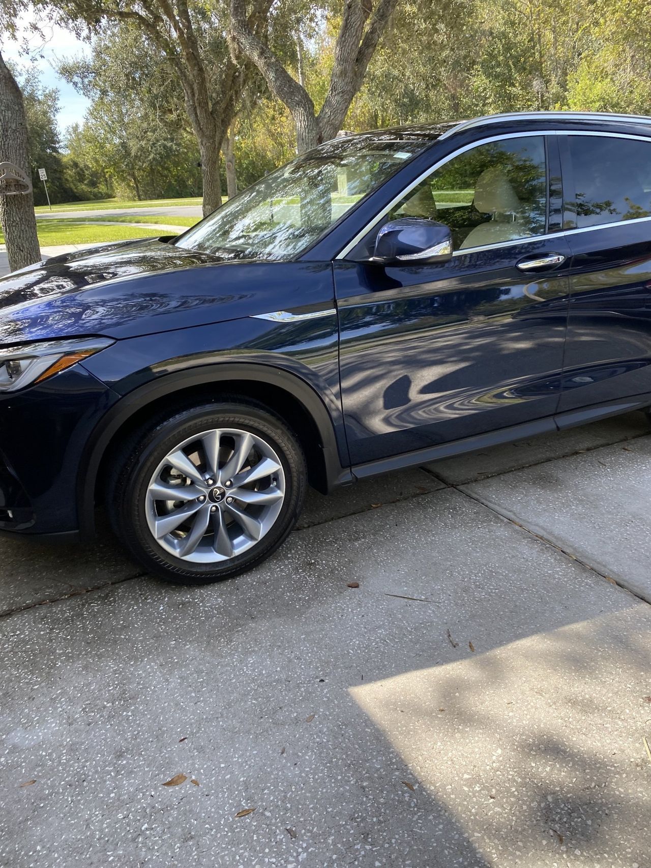 A blue car is parked in a driveway next to trees.