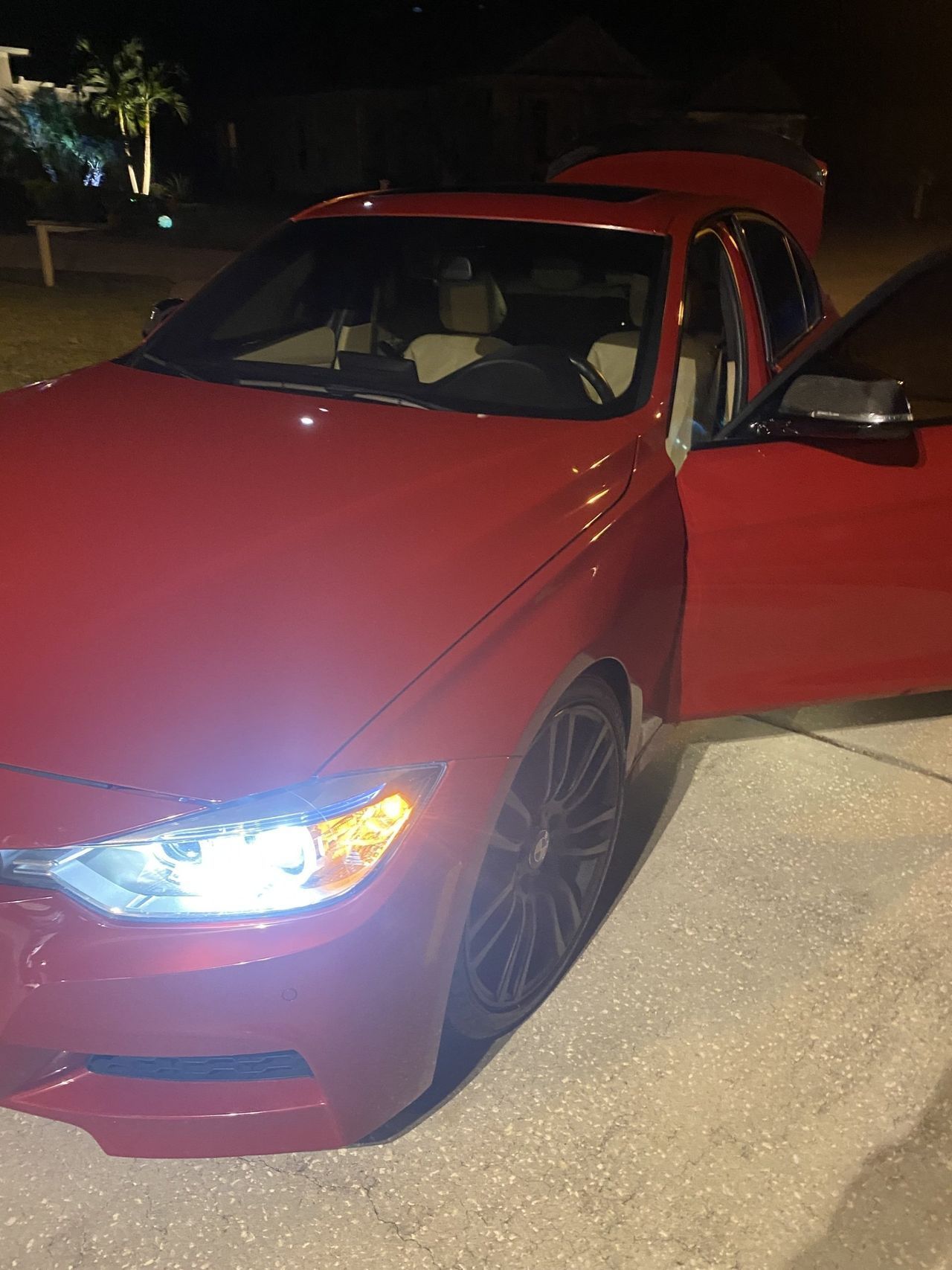 A red car is parked on the side of the road at night.