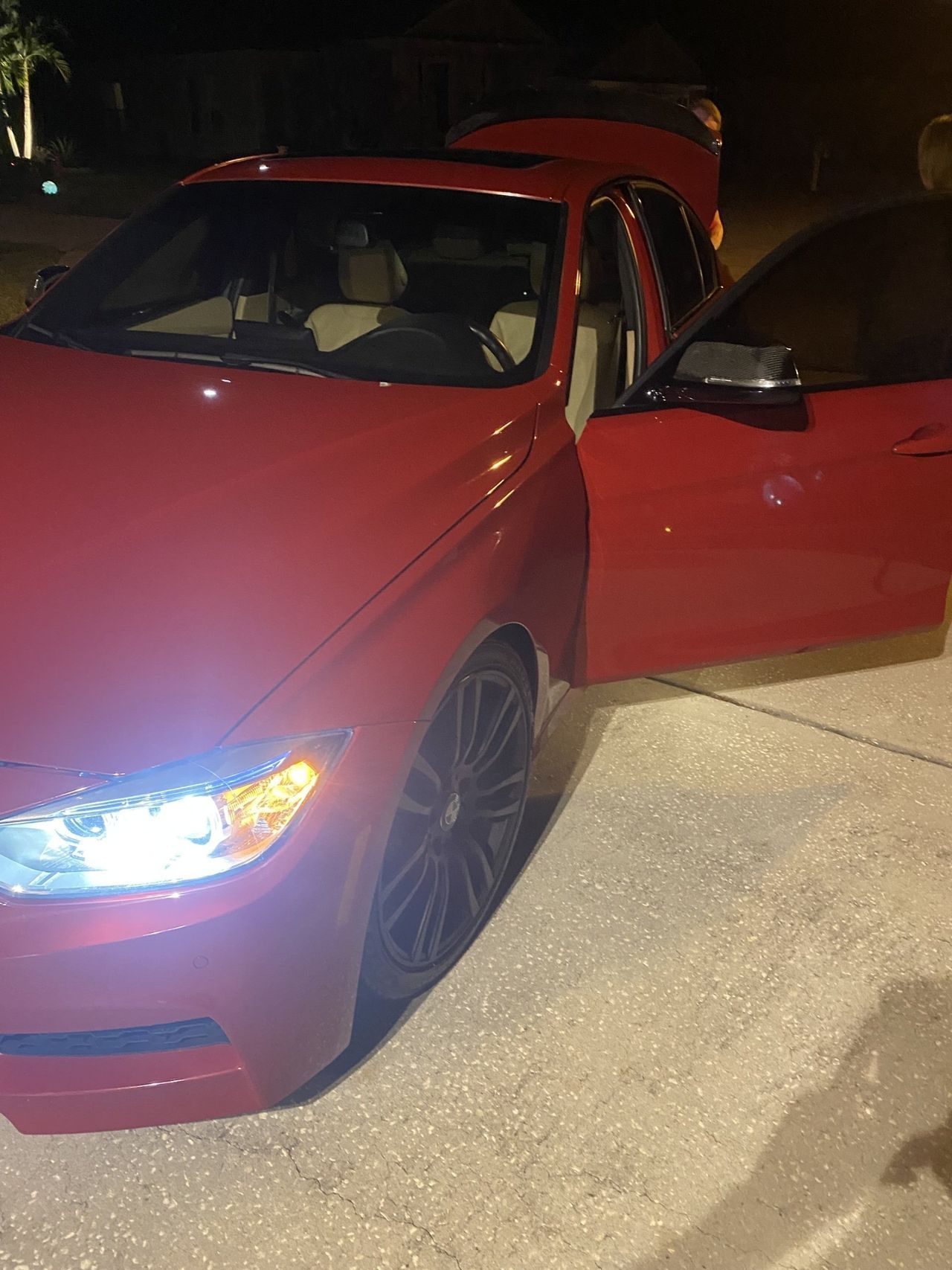 A red car is parked in a driveway at night with the door open.