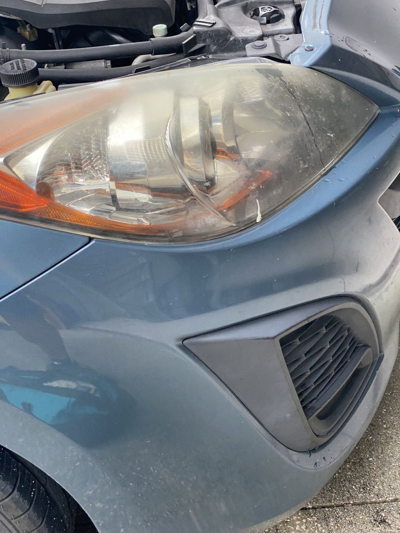 A close up of a car 's headlight with the hood open.