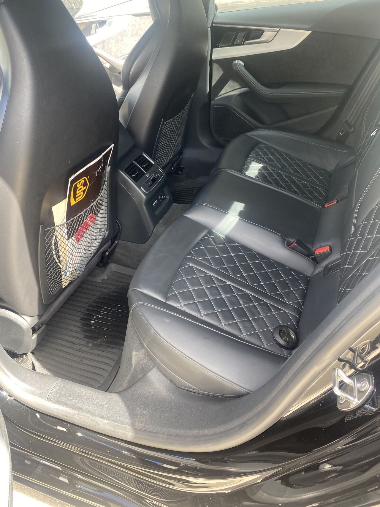 The back seat of a black audi a4 is shown with the door open.
