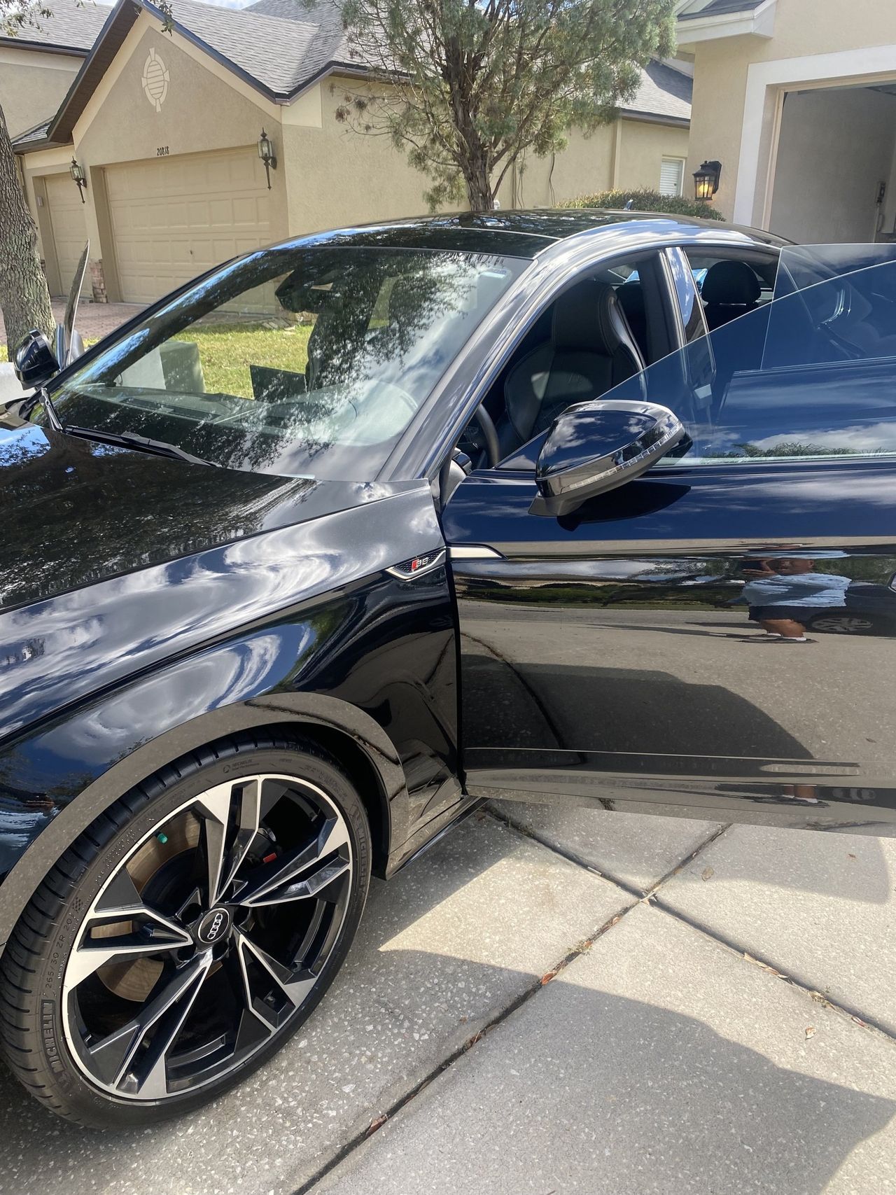 A black car is parked in a driveway in front of a house.