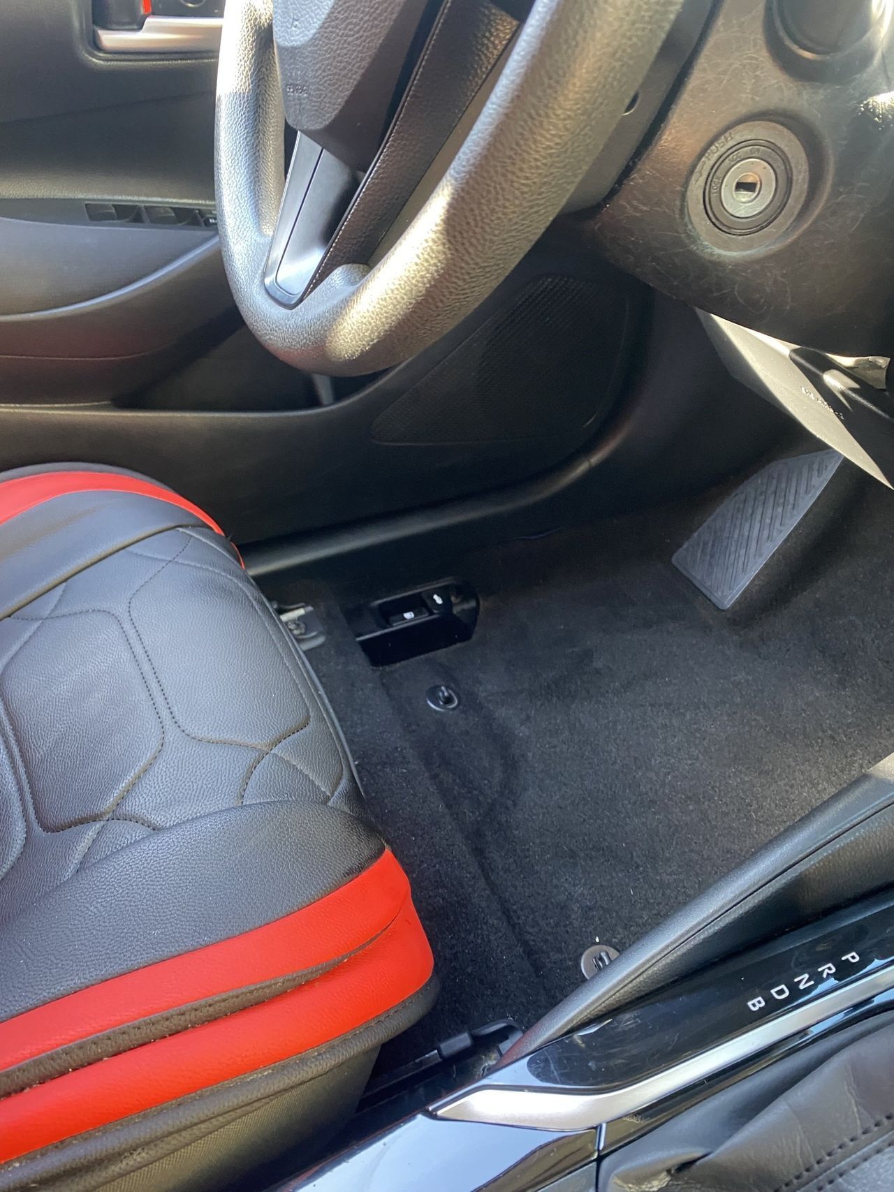 The inside of a car with a steering wheel and a red seat cover.