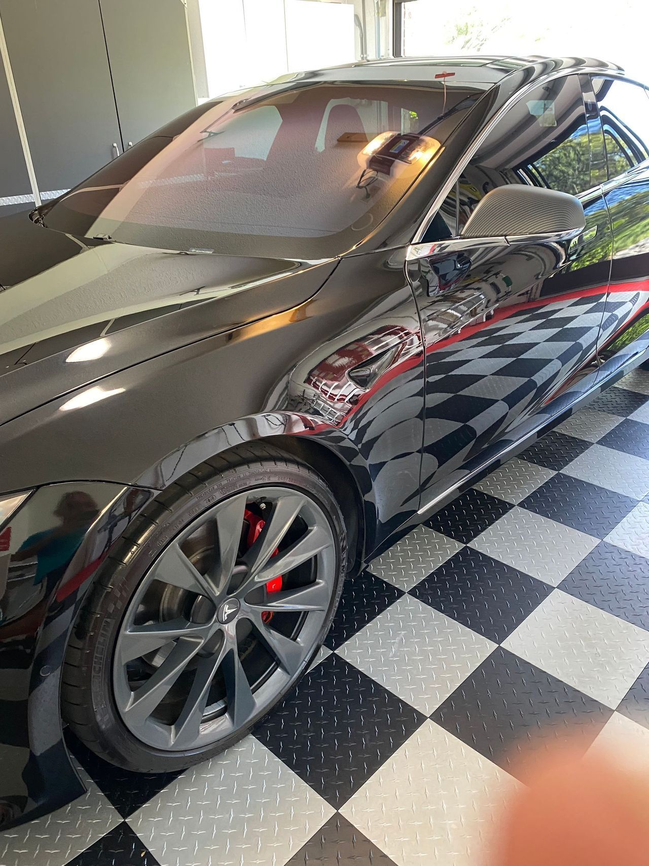 A black car is parked in a garage on a checkered floor.