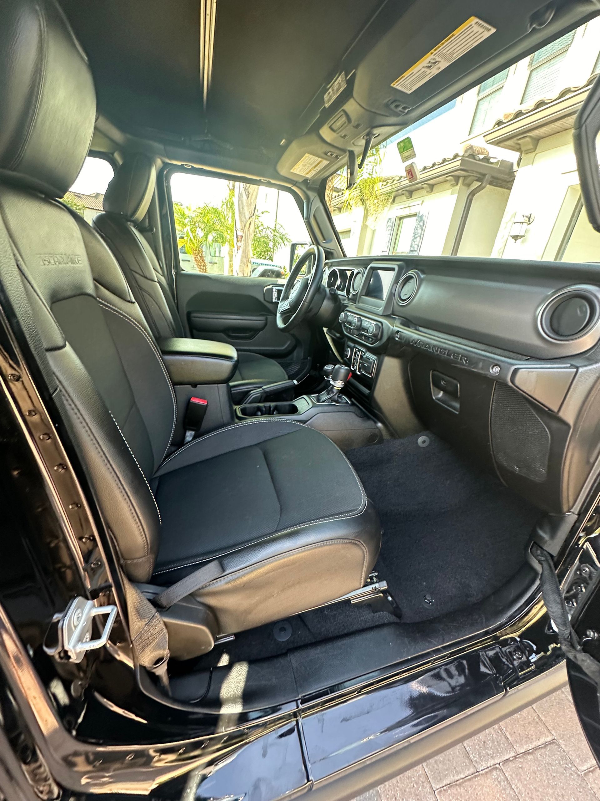 The interior of a black jeep wrangler is shown with the door open.
