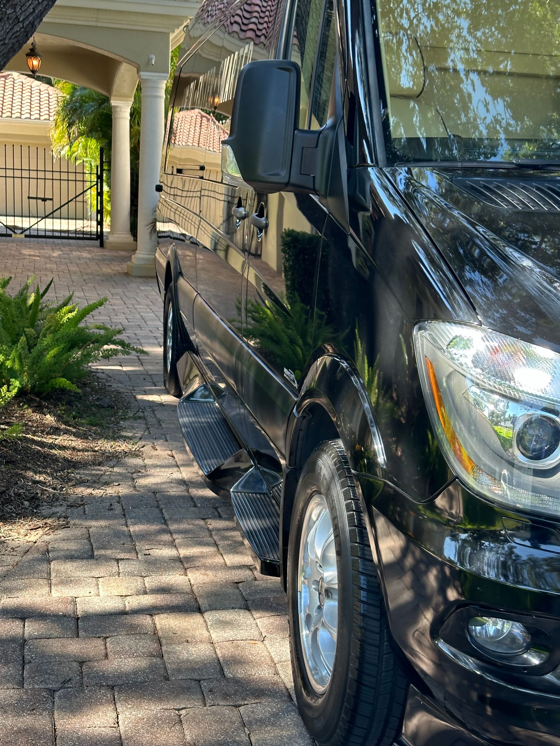 A black van is parked on a brick sidewalk in front of a house.