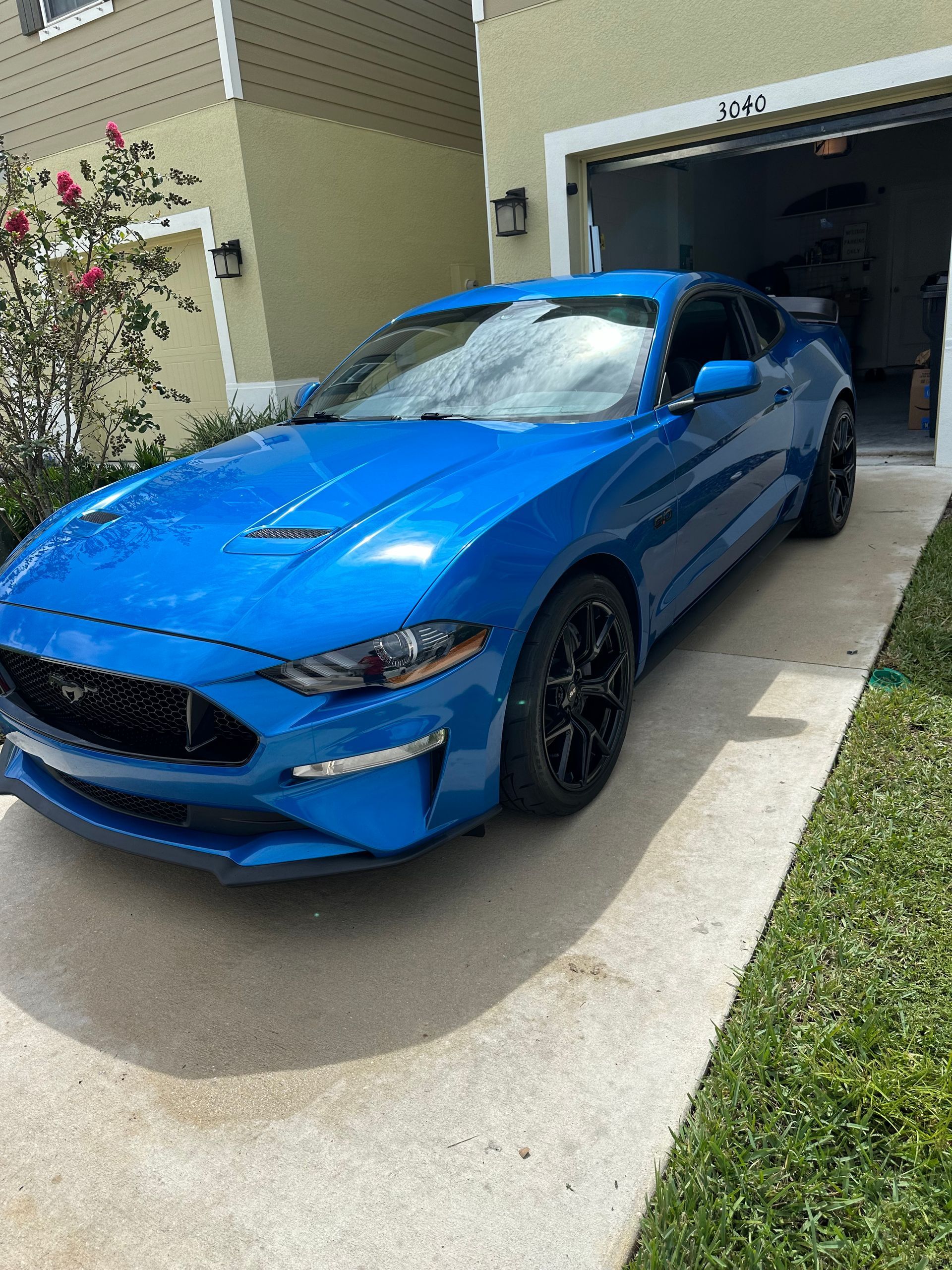 A blue Mustang is parked in front of a garage