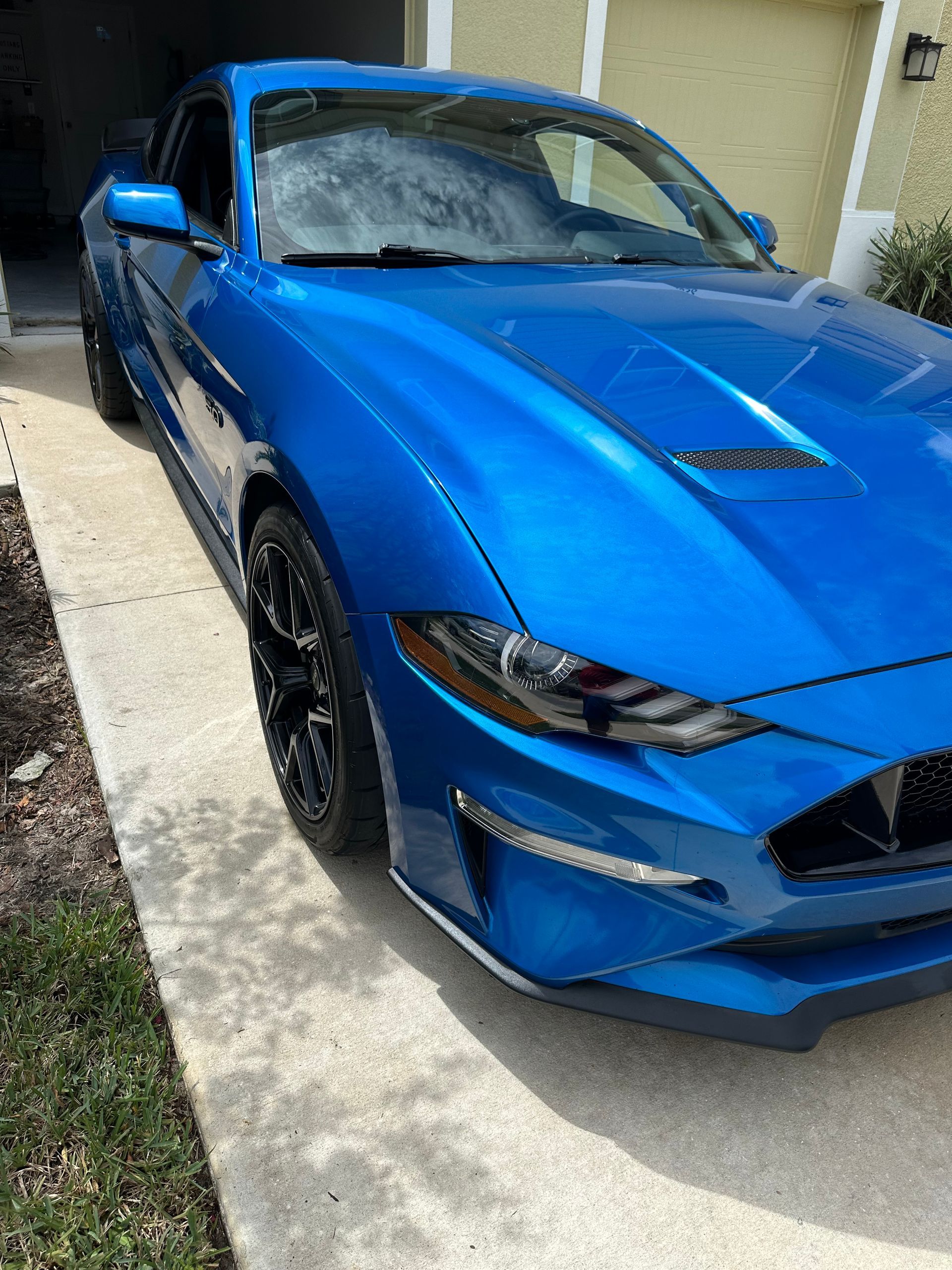 A blue Mustang is parked in a driveway next to a house