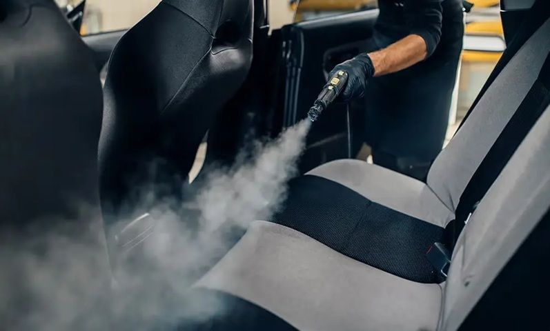A person steam cleaning a car seat in a garage.