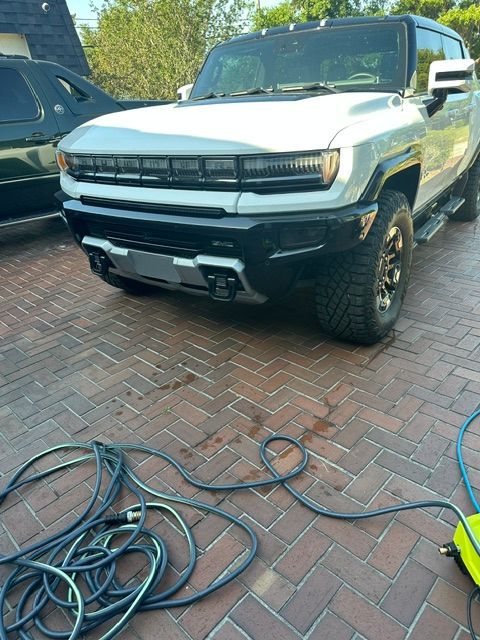 A white hummer is parked on a brick driveway next to a hose.