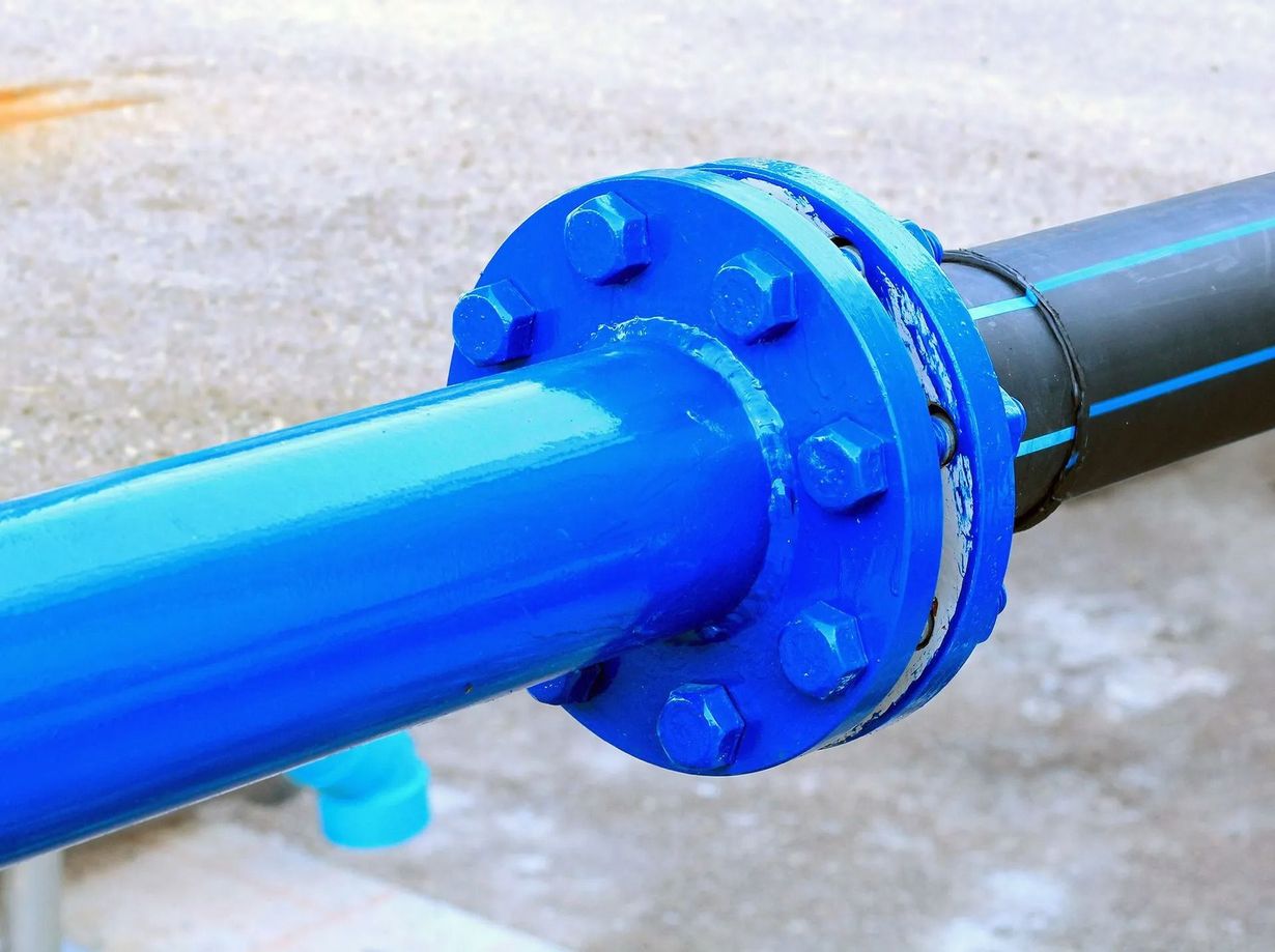 Blue painted pipe section connected to a black pipe with a bolted flange. Outdoor setting.