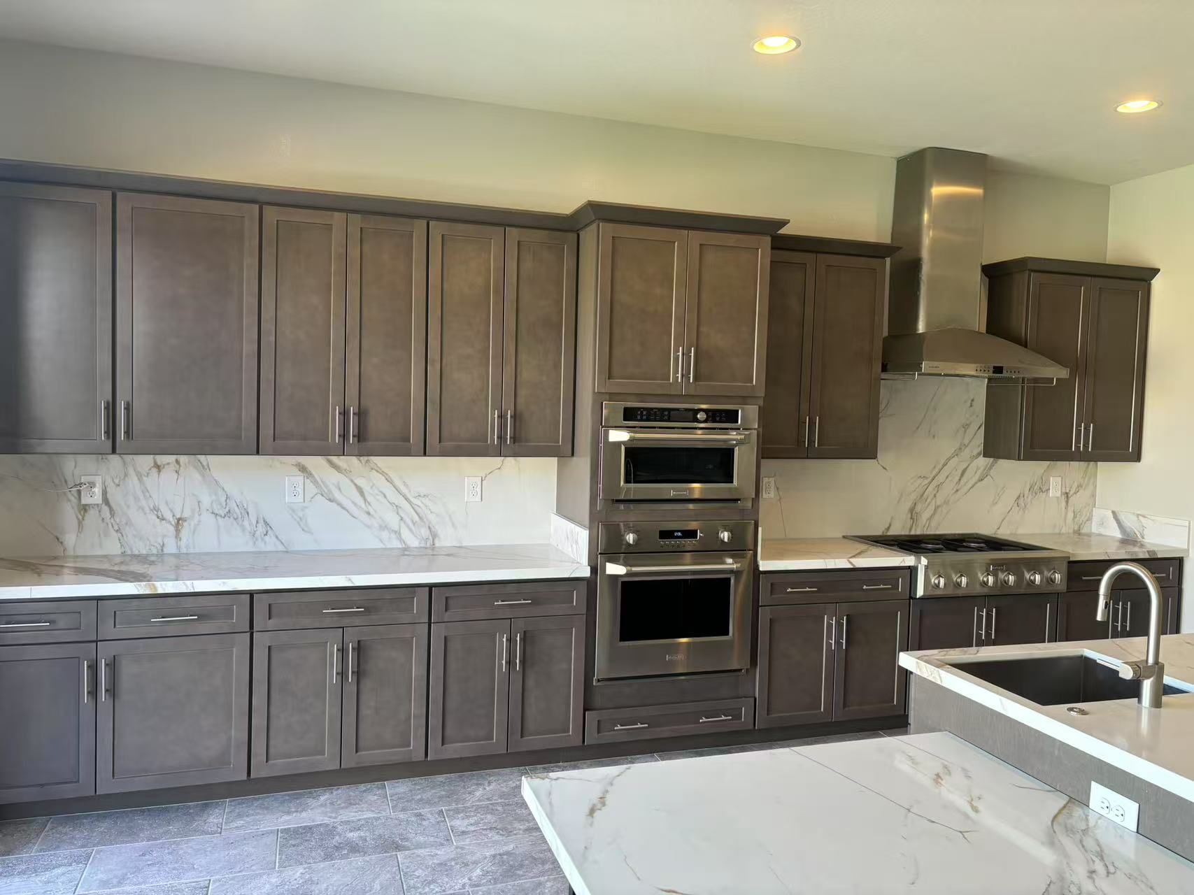 A modern kitchen with dark brown cabinets, white marble countertops, and stainless steel appliances.